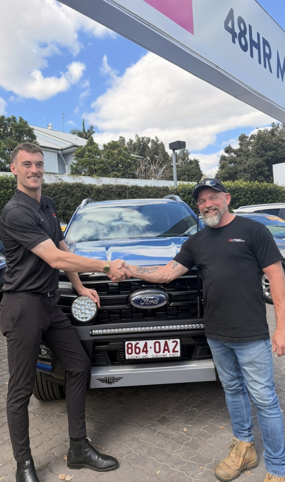 Liam O’Connor shaking hands beside a Ford vehicle at a dealership