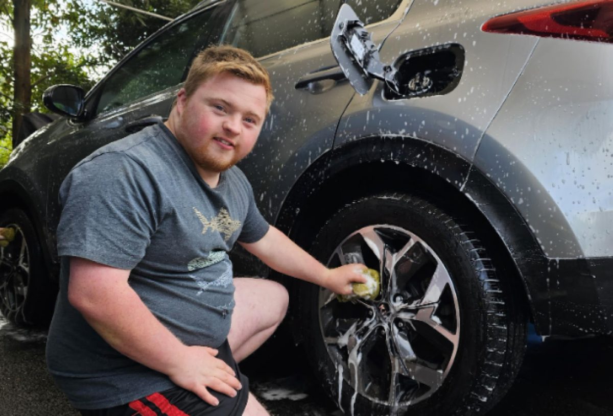 Person washing a car beside a parked vehicle outdoors